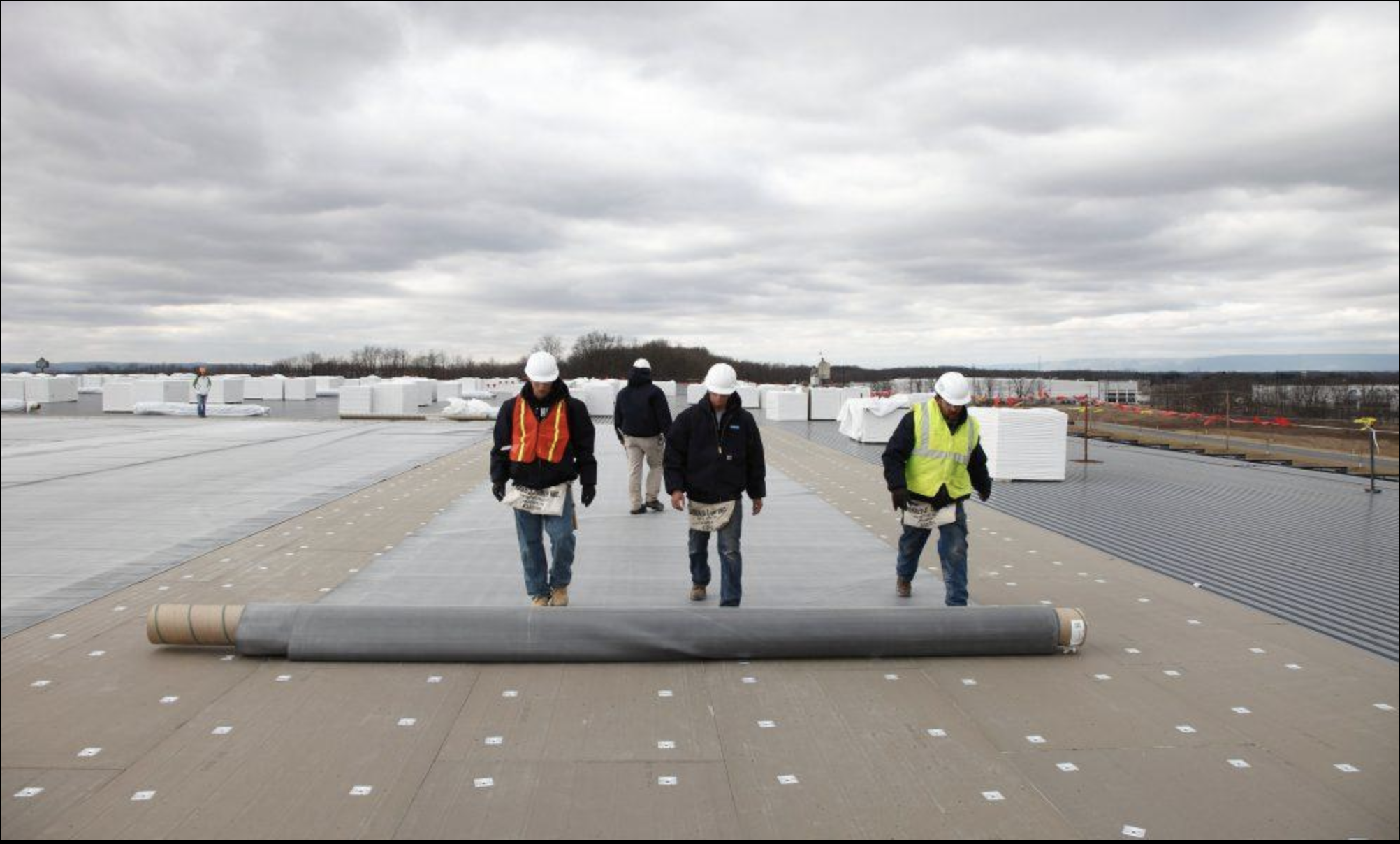 Construction workers inspecting a rooftop during overcast weather, with equipment and materials around.