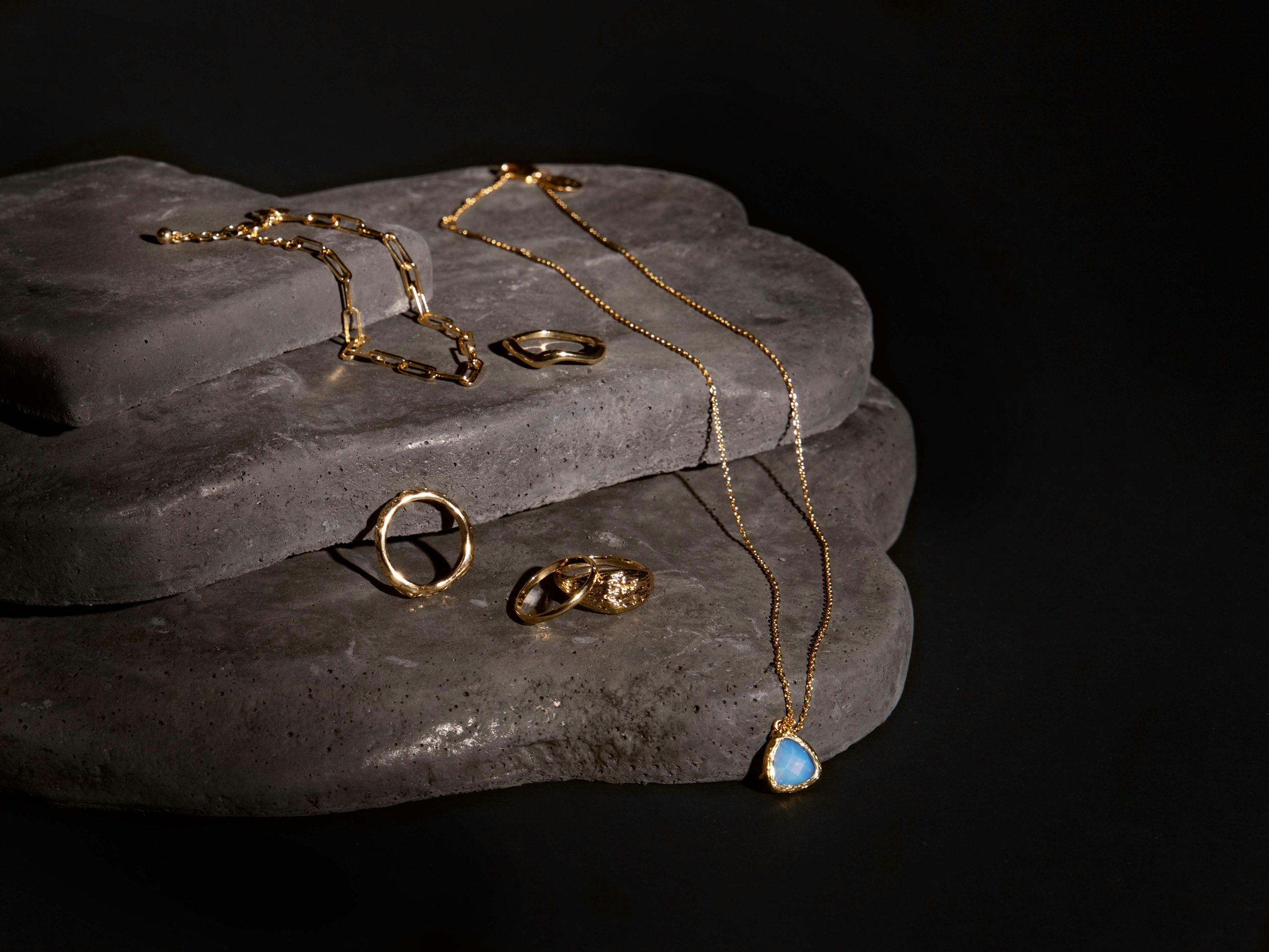 Gold jewelry including rings, necklaces, and a bracelet displayed on dark stone slabs.