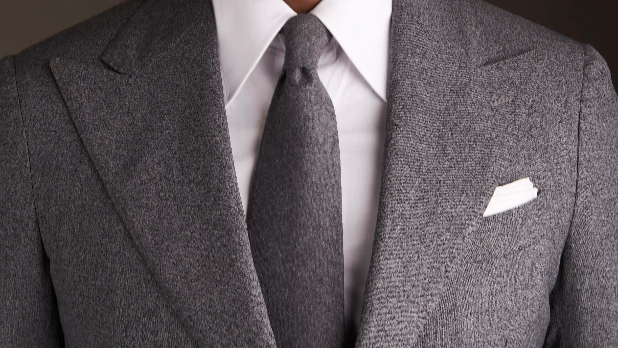 Close-up of a man wearing a gray suit, white shirt, gray tie, and white pocket square.