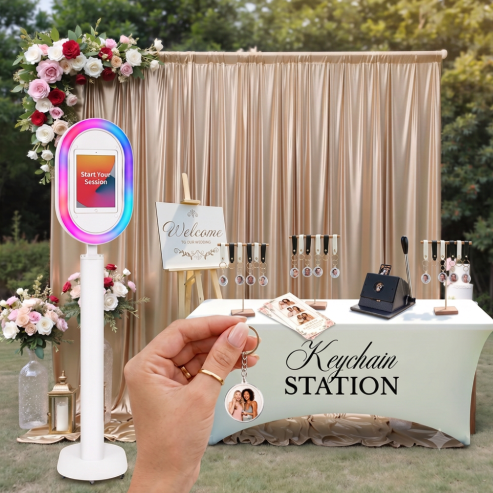 A wedding keychain station setup with a sign that says "Welcome to our wedding," a table with various keychains, and a hand holding a keychain with a photo of two women. The backdrop includes a gold curtain and floral arrangements.