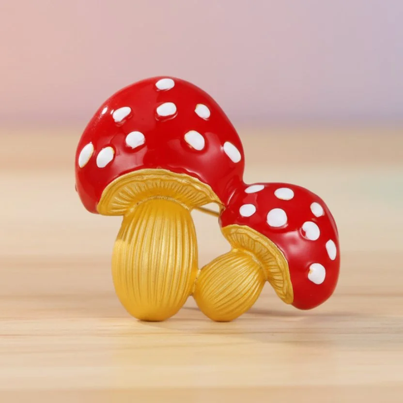 Red and gold double mushroom brooch on a pastel pink background