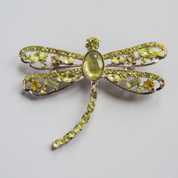 Green gemstone and rhinestone dragonfly brooch on white background.