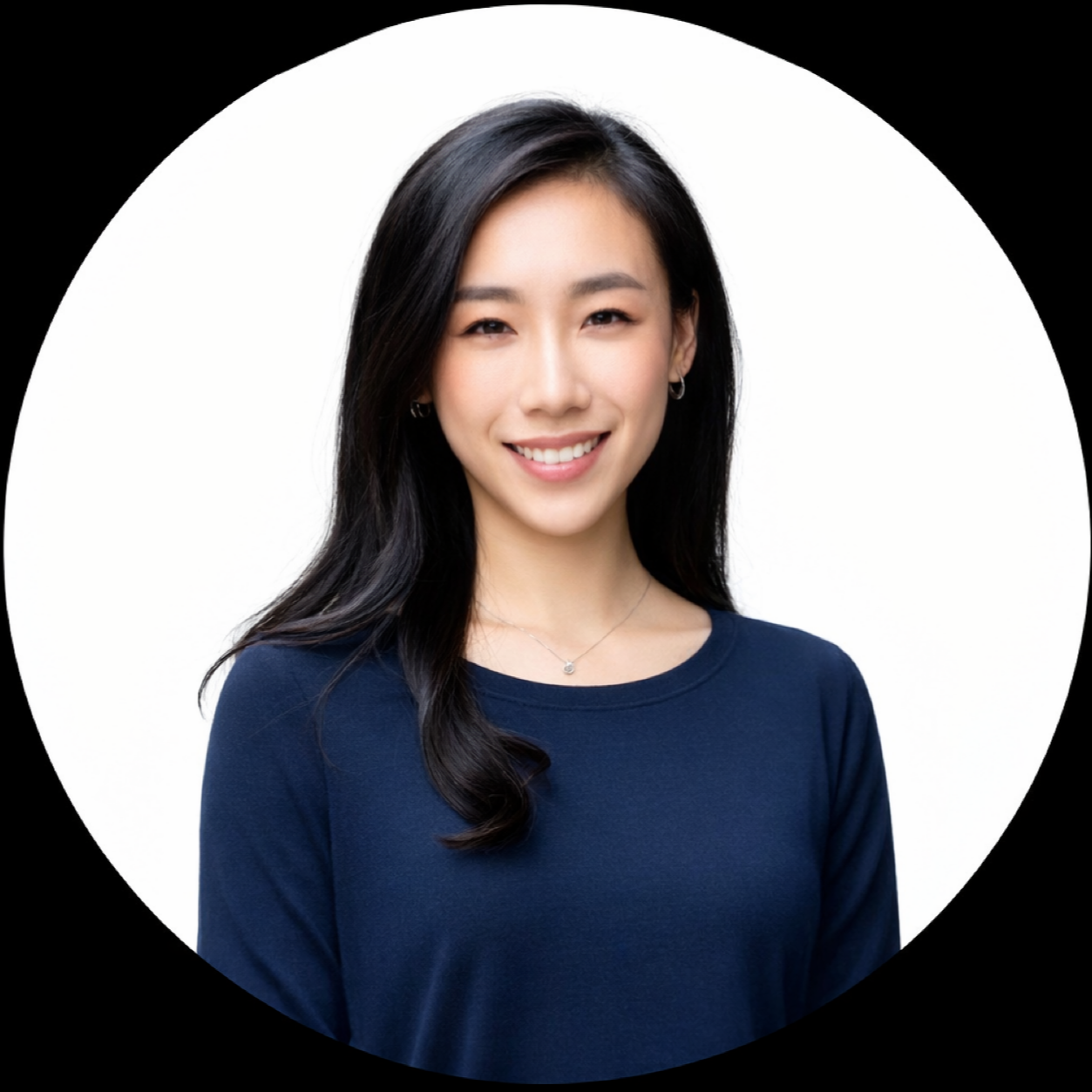 A woman with long black hair, wearing a navy blue top, smiling, with small hoop earrings and a delicate necklace, in front of a white background with a black circular border.