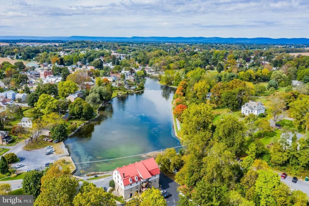 Aerial view of a small town with houses, trees, and a river running through it on a partly cloudy day.