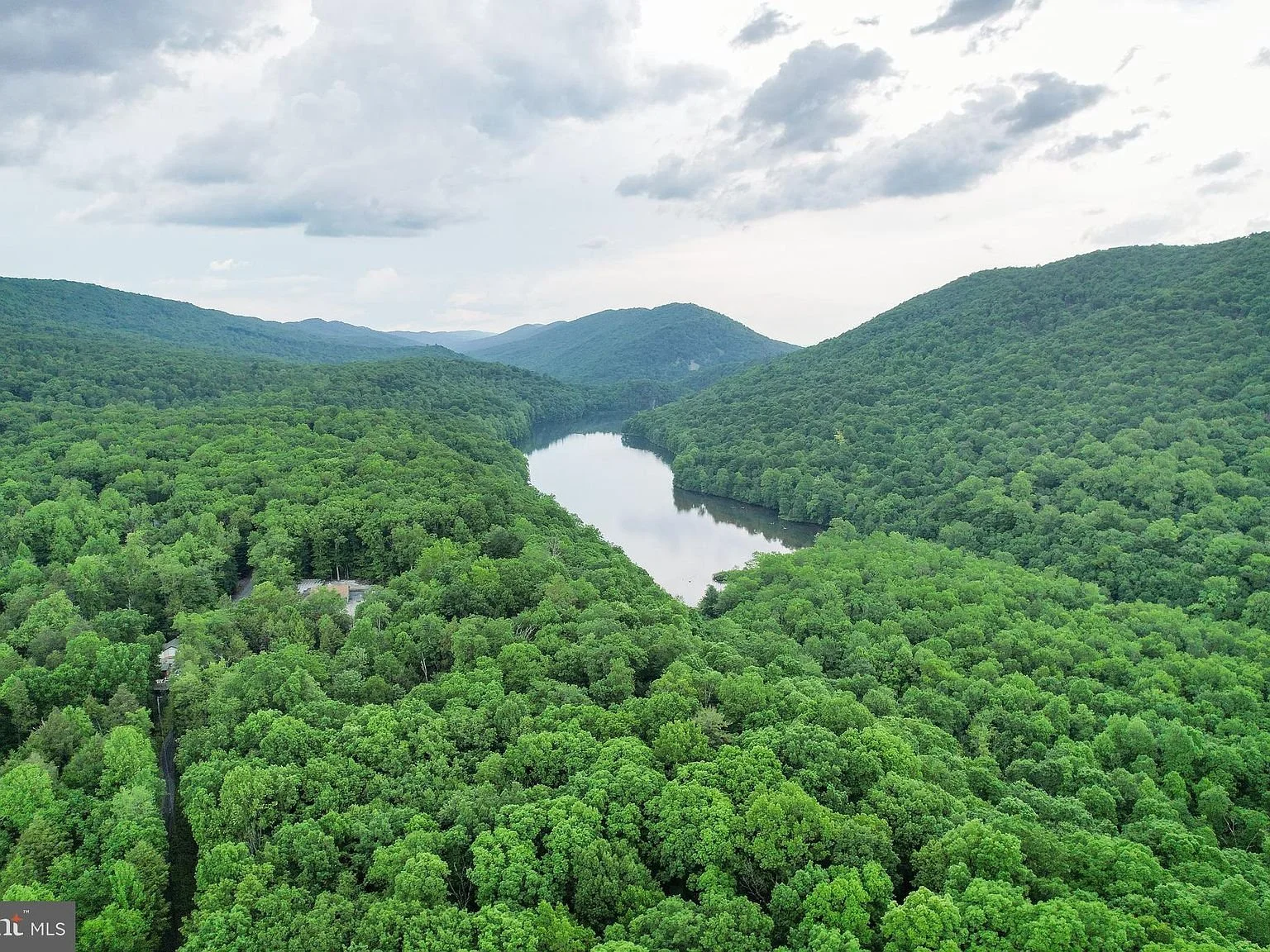 Aerial view of a winding river flowing between densely forested green hills under a cloudy sky.