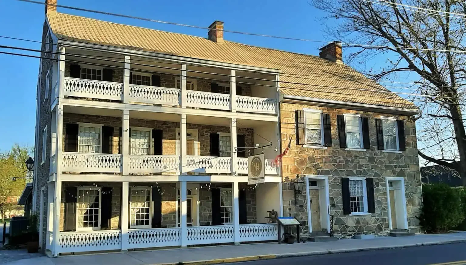 Three-story stone building with white balconies and black shutters, next to a leafless tree during daytime.