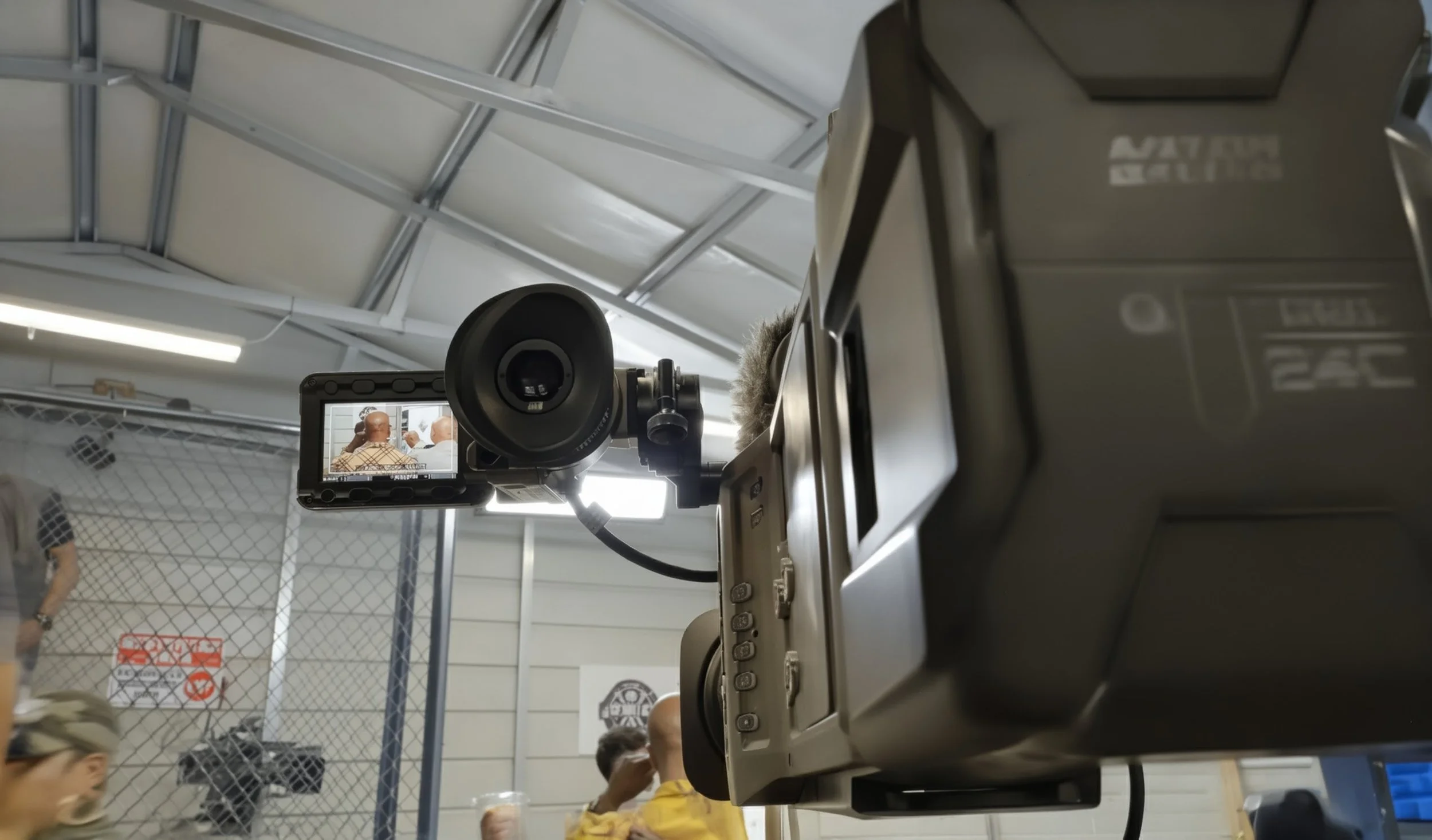 A professional video camera recording a scene at an indoor event, with people in the background.