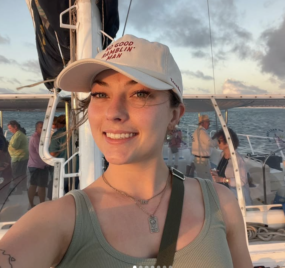 A woman taking a selfie on a boat with other people in the background, during sunset with cloudy skies over the ocean.