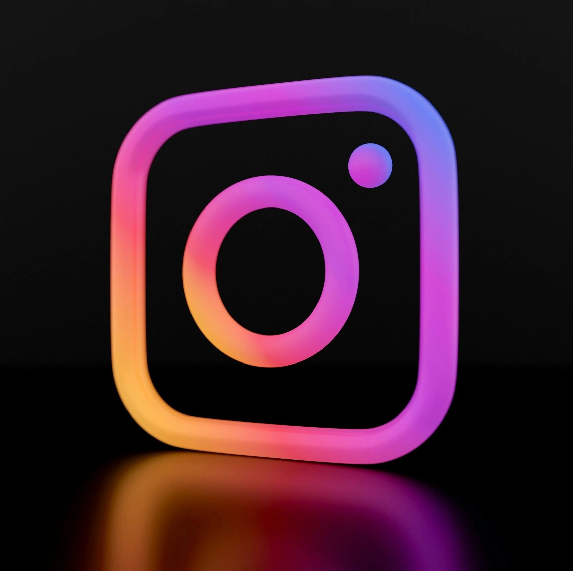 Close-up of a neon sign with colorful concentric circles and a rounded square, glowing in shades of pink, purple, orange, and violet against a black background.
