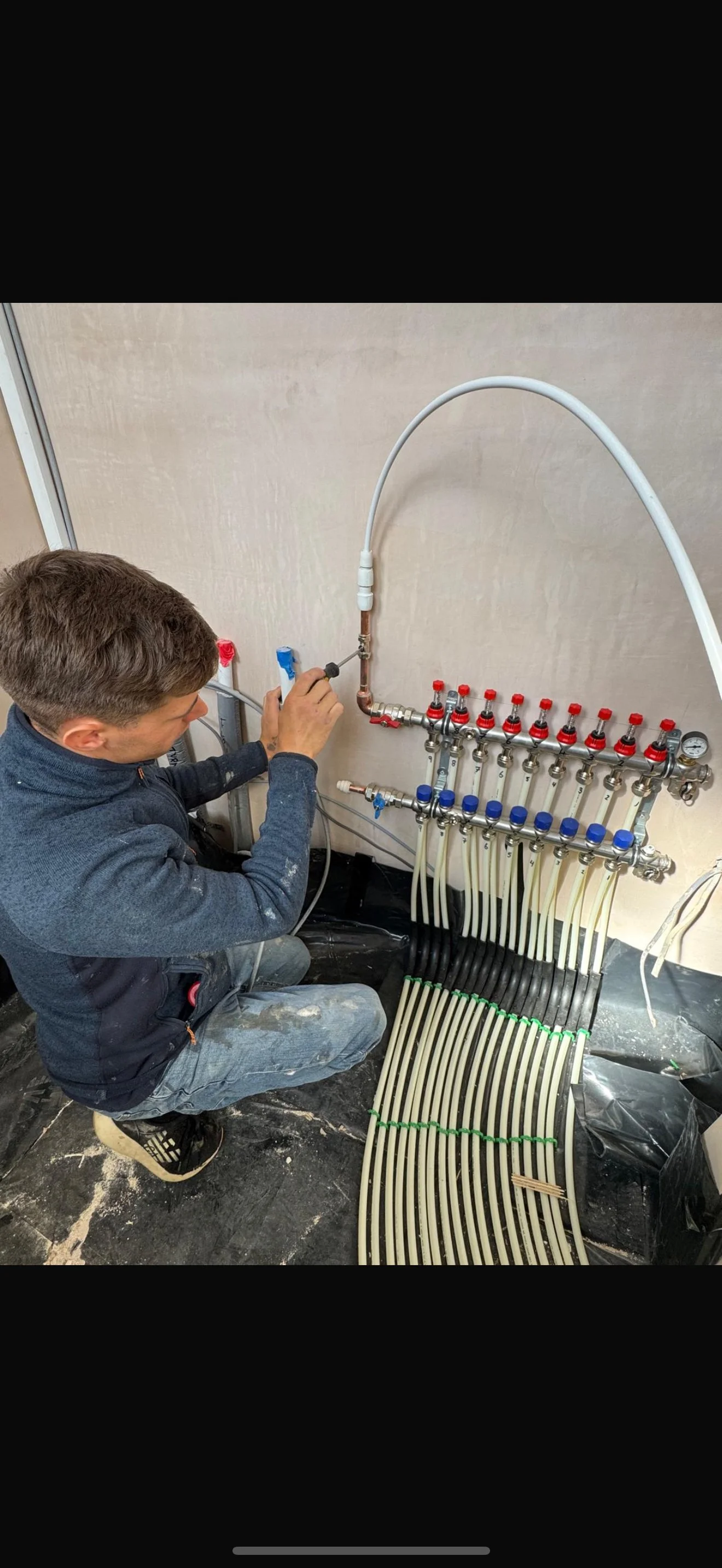 A person working on a plumbing system with multiple pipes, valves, and a manifold, possibly installing or repairing it in a construction or renovation setting.