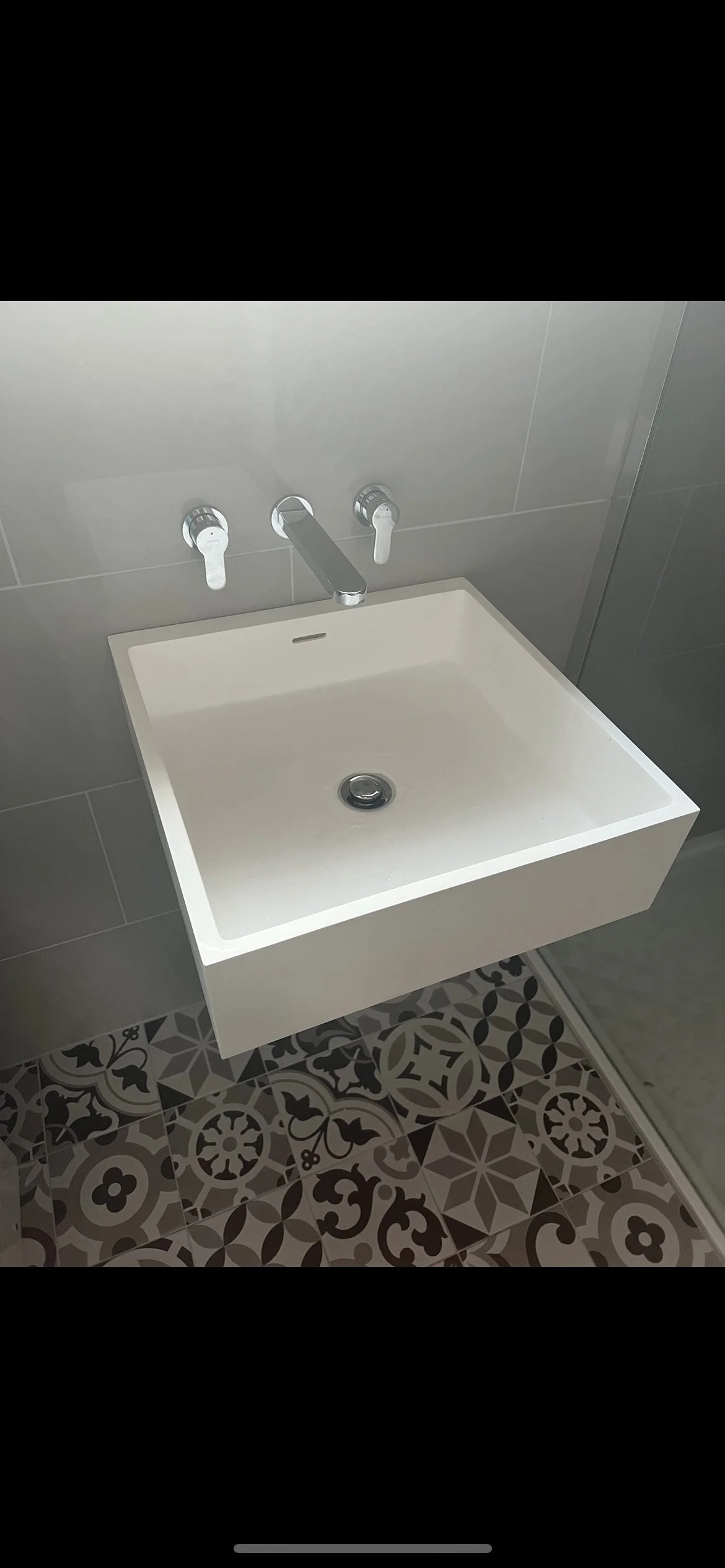 Modern white bathroom sink with wall-mounted faucet and patterned floor tiles.