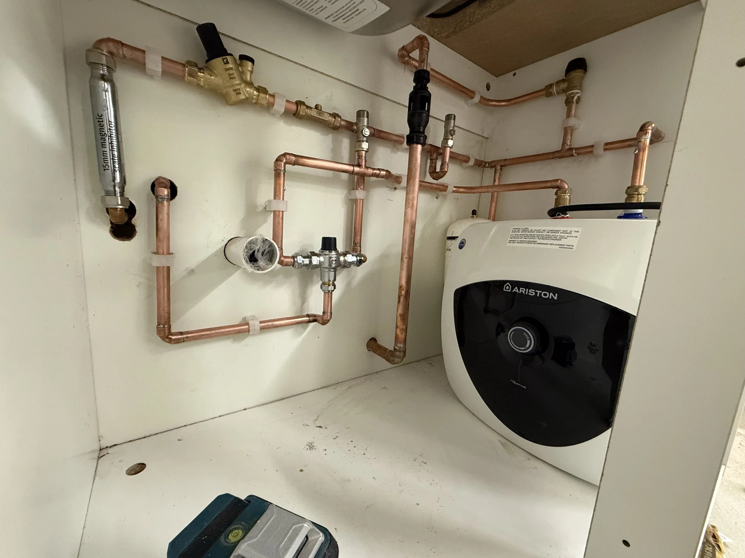 Inside a cabinet with copper pipes, a brass valve, a water heater, and a level tool on the floor.