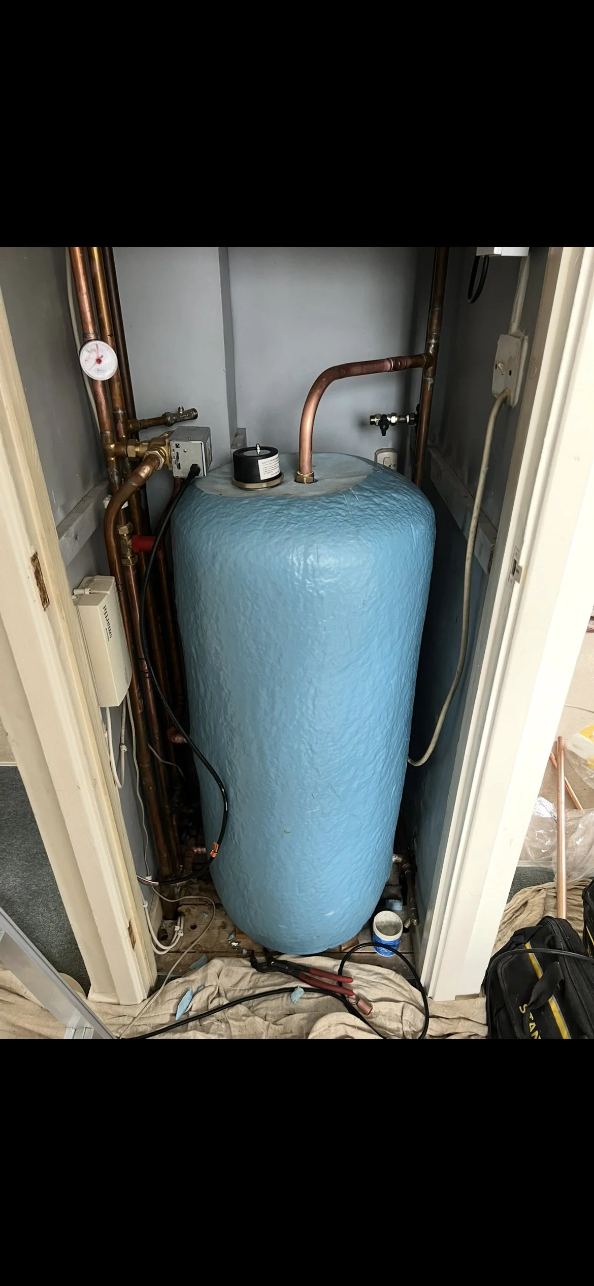 A water heater with various plumbing pipes and electrical connections inside a small closet.