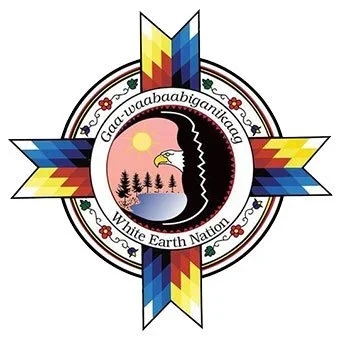 A circular emblem with four colorful geometric shapes extending outward, featuring a Native American style design. Inside the circle, there is a black silhouette of a face with a landscape including trees, water, a yellow sun, and an eagle's head. Text around the circle reads 'Gaa-waababaabgquing' and 'White Earth Nation.'