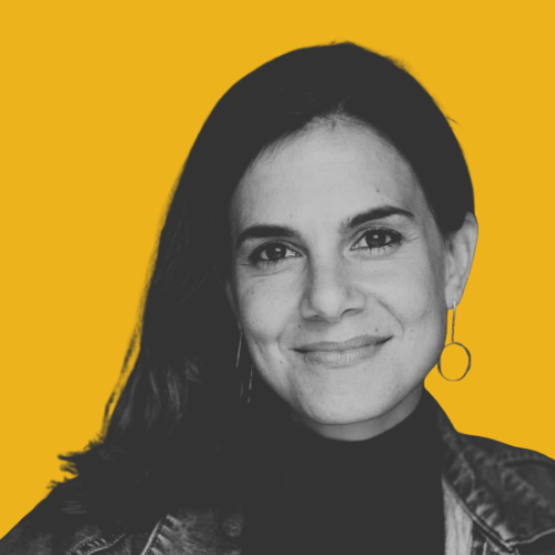 Portrait of a smiling person with long, dark hair, and metal earings with hoops on chains.