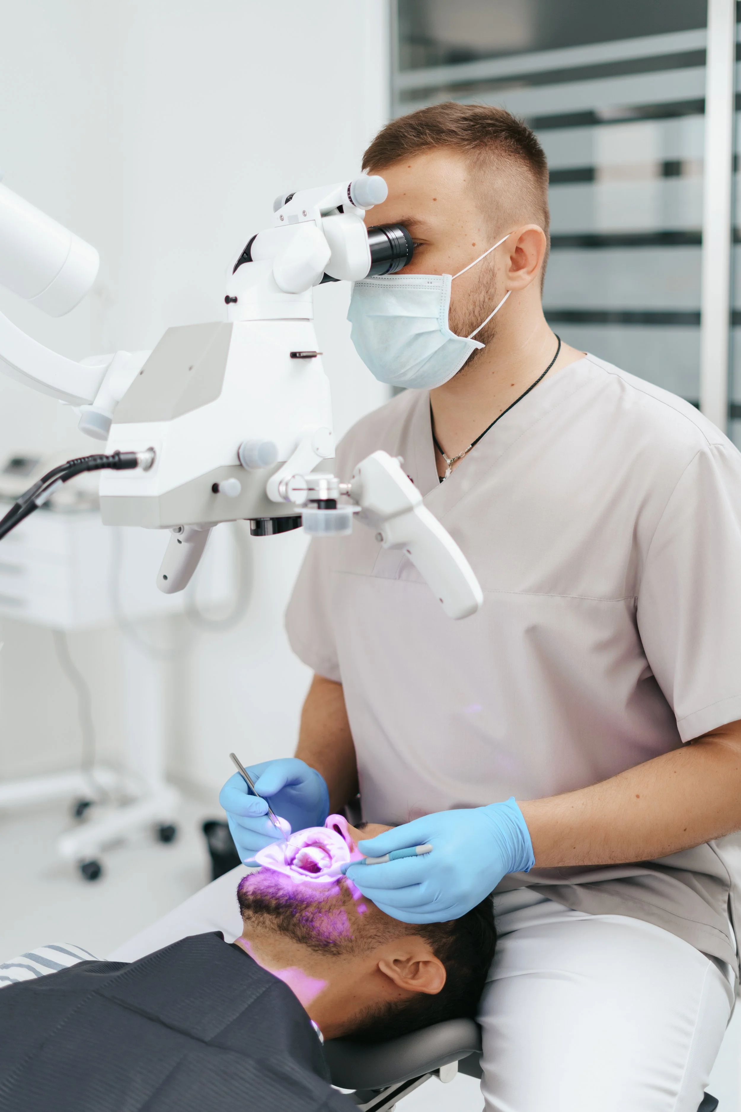Dentist examining patient's teeth using specialized dental equipment in a clinical setting.