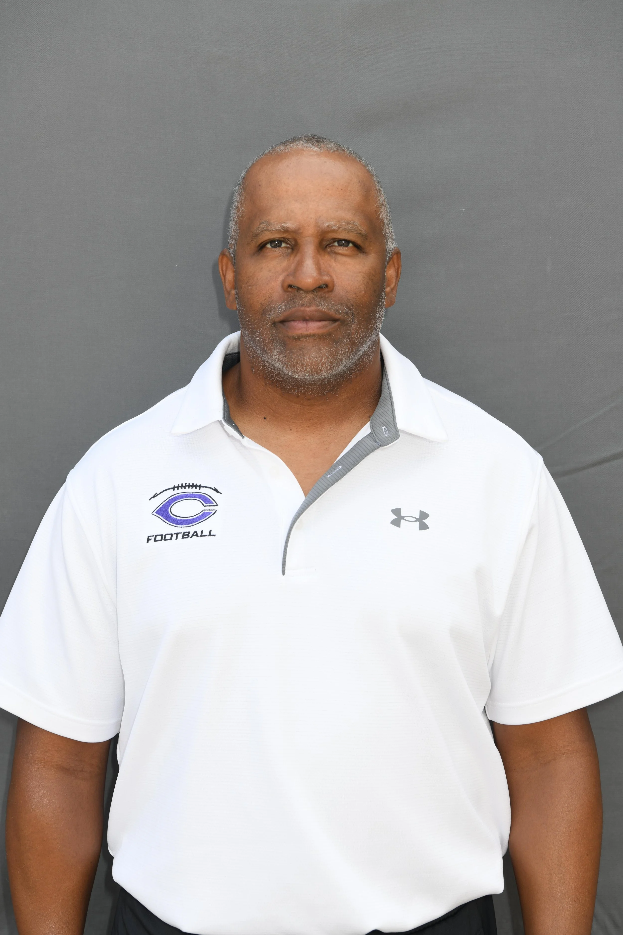 Man wearing a white football coaching shirt standing against a gray background.