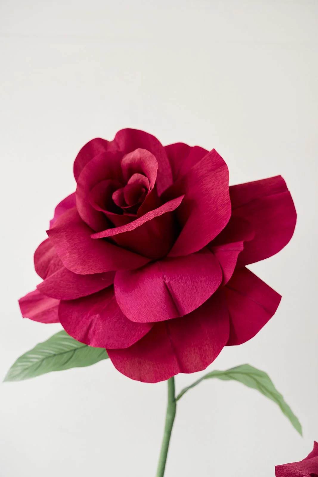Close-up of a pink artificial rose with green leaves against a plain light background.