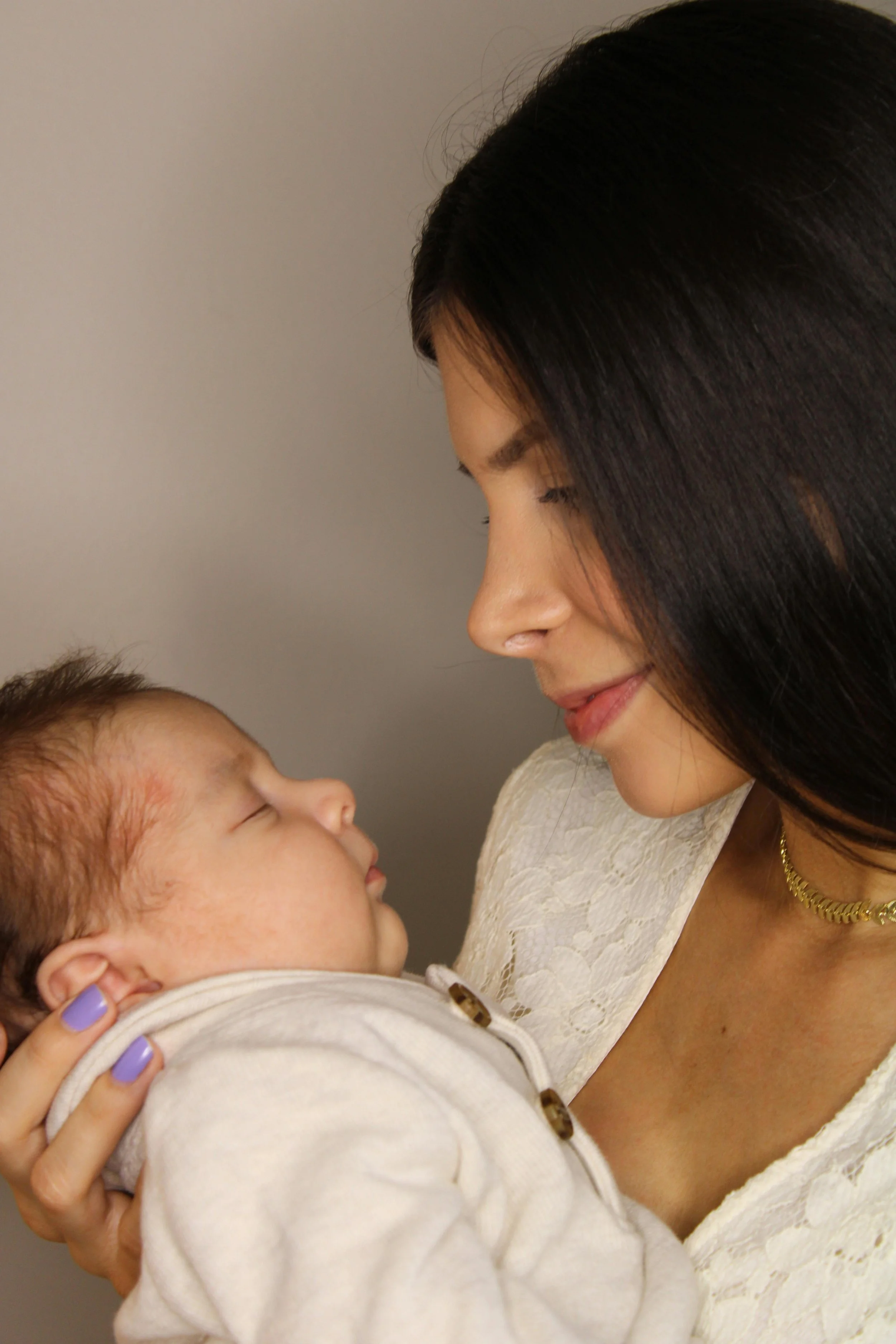 A woman and a young child look at each other closely, with the woman smiling gently and the child sleeping, showing a tender moment of connection.