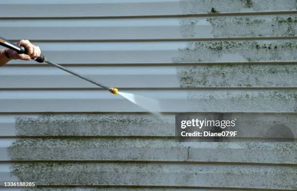 Person pressure washing a dirty exterior wall with a high-pressure spray.
