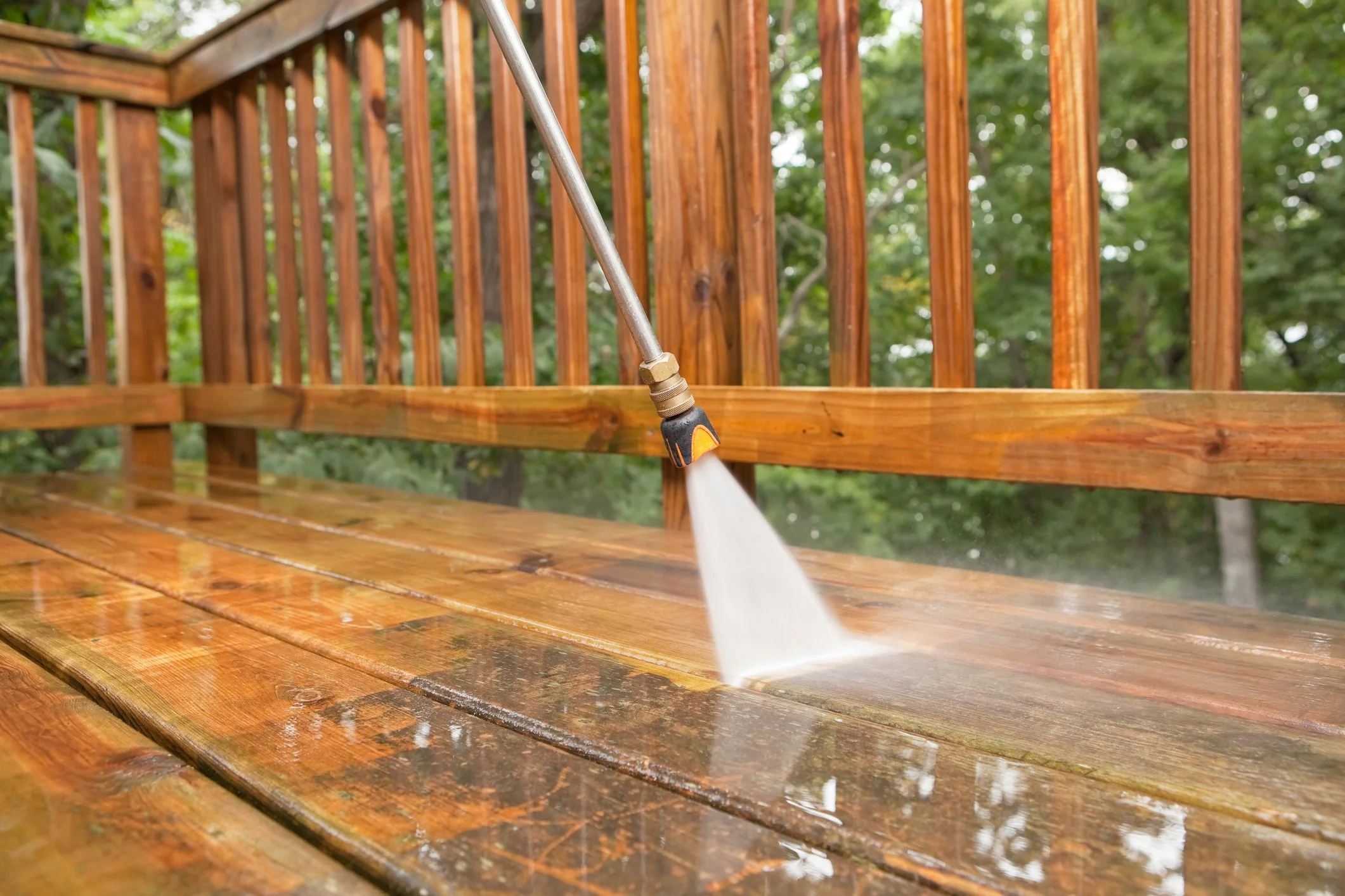 A pressure washer cleaning a wooden outdoor deck with a spray of water.