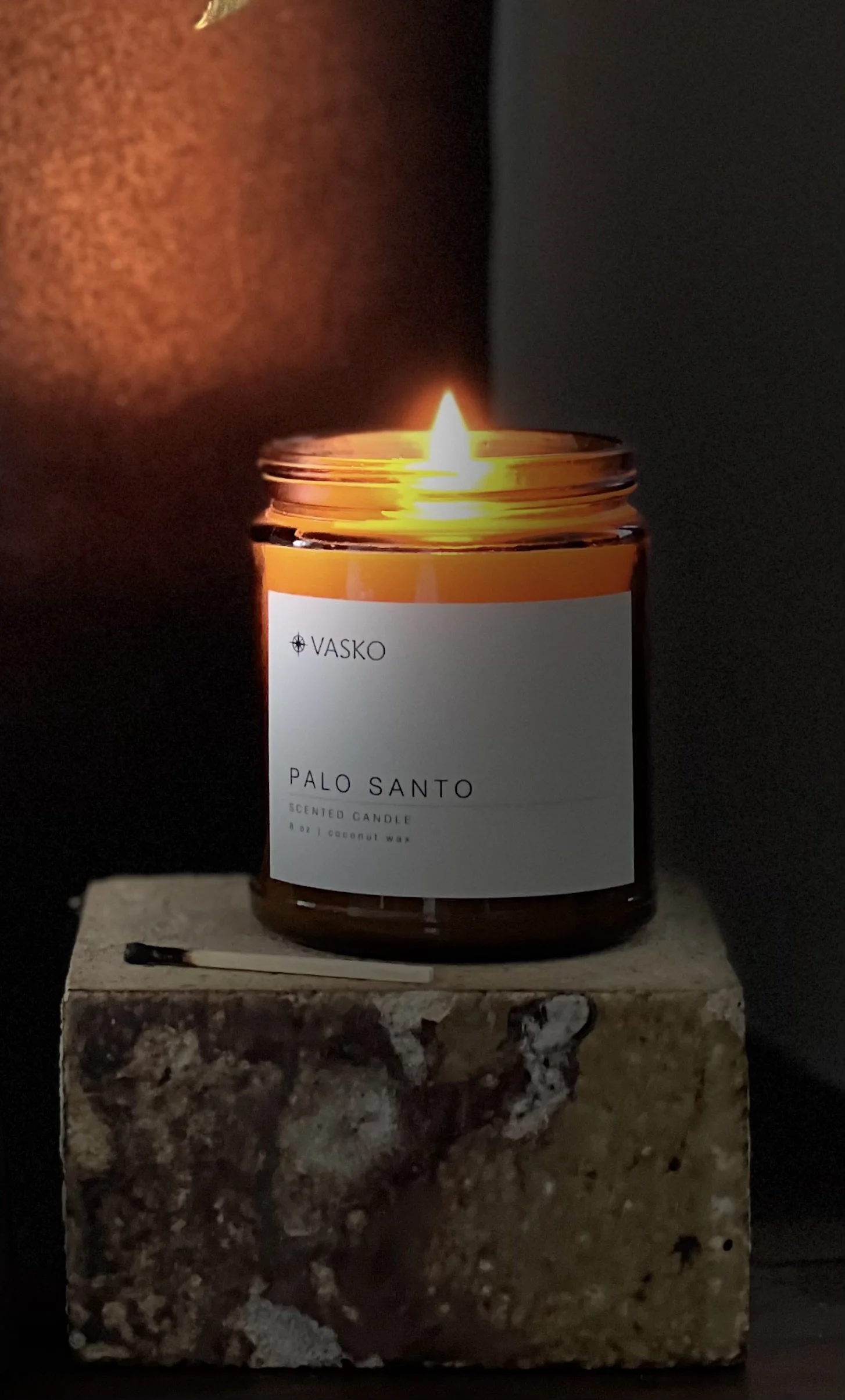 A lit scented candle labeled 'Palo Santo' in a dark room, placed on a stone surface.