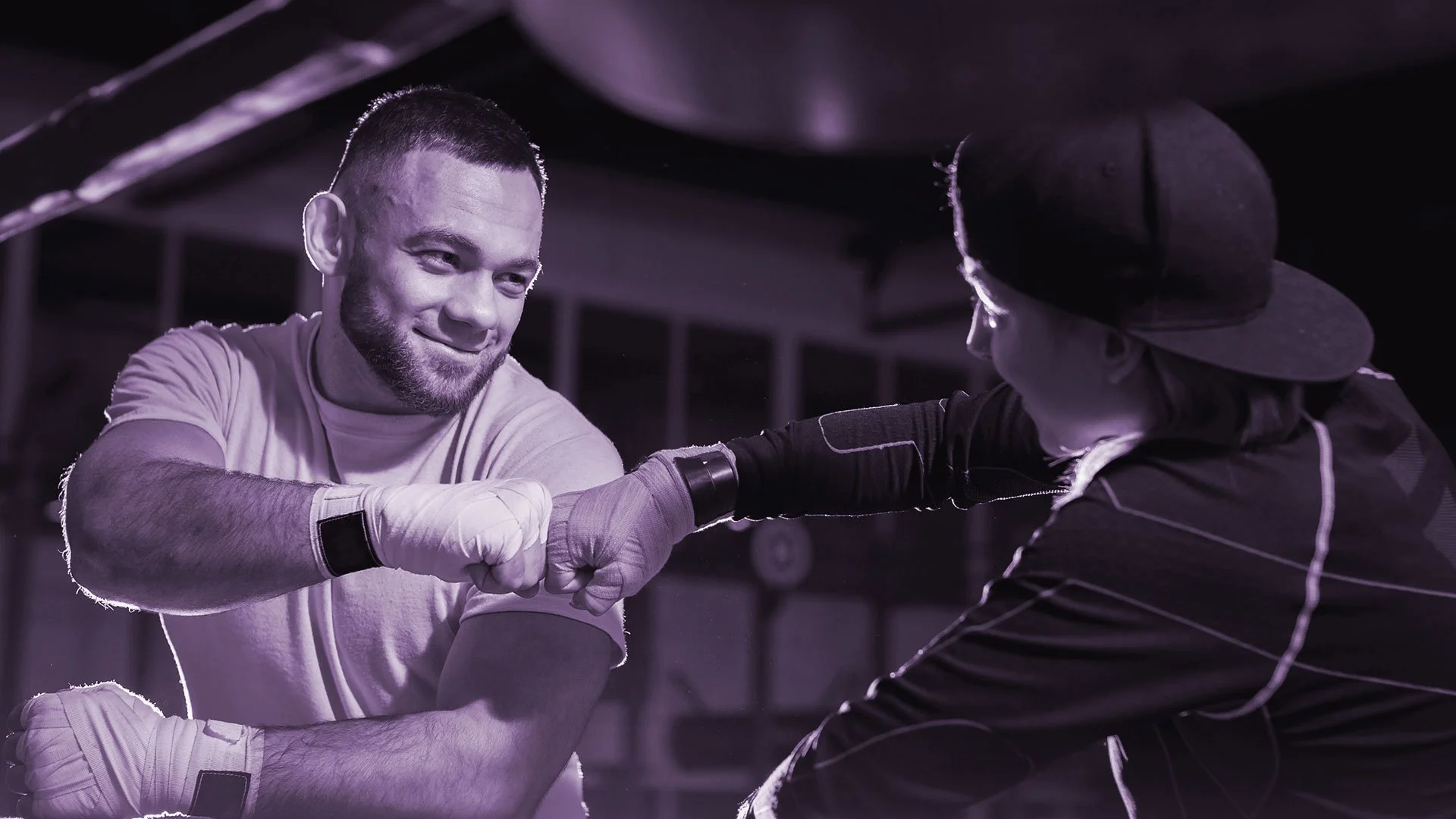 Dos personas con ropa deportiva y guantes de boxeo dándose un choque de puños en un gimnasio