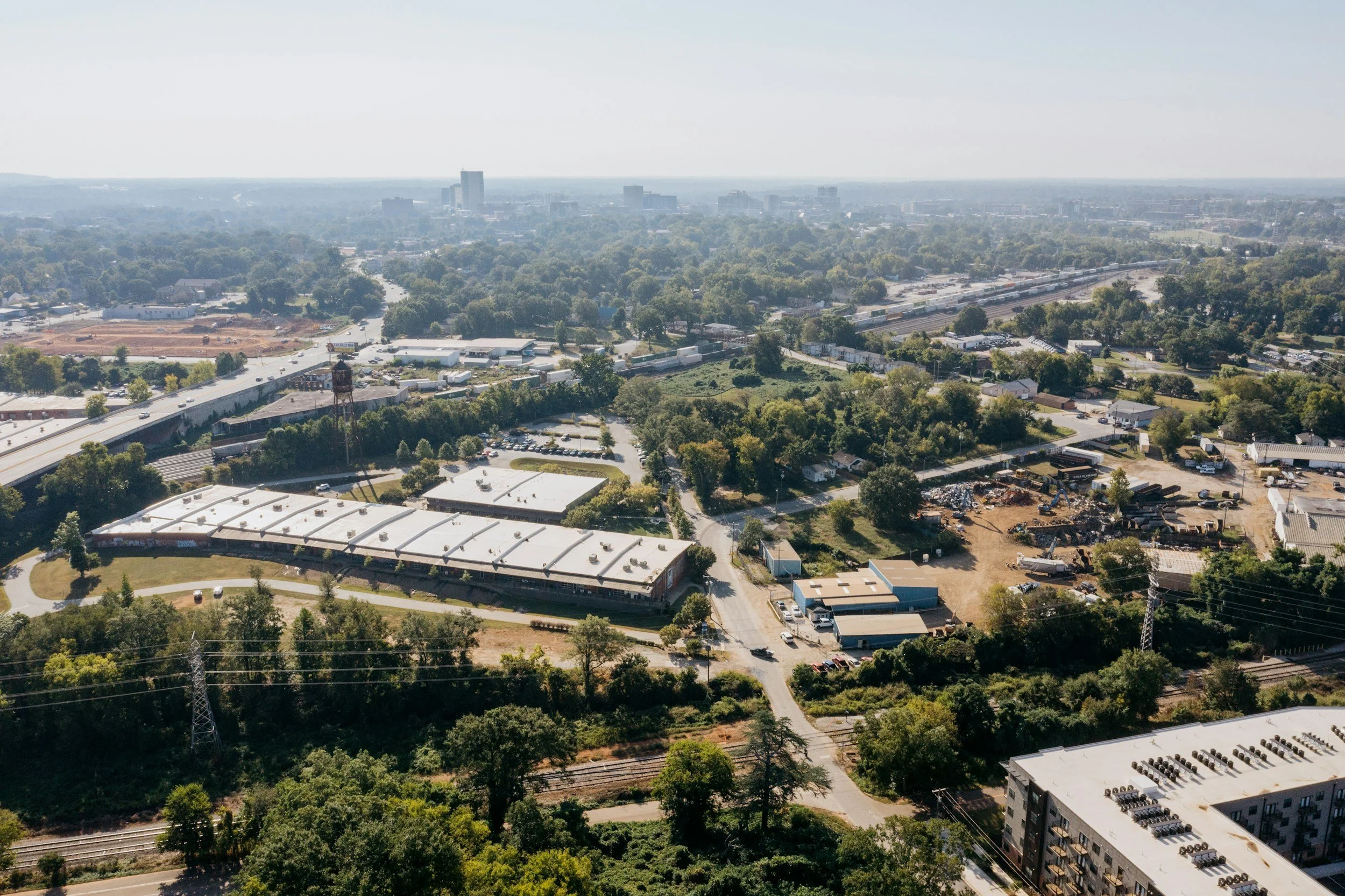 An aerial view of a city landscape showing trees, roads, and buildings with a hazy skyline in the background.