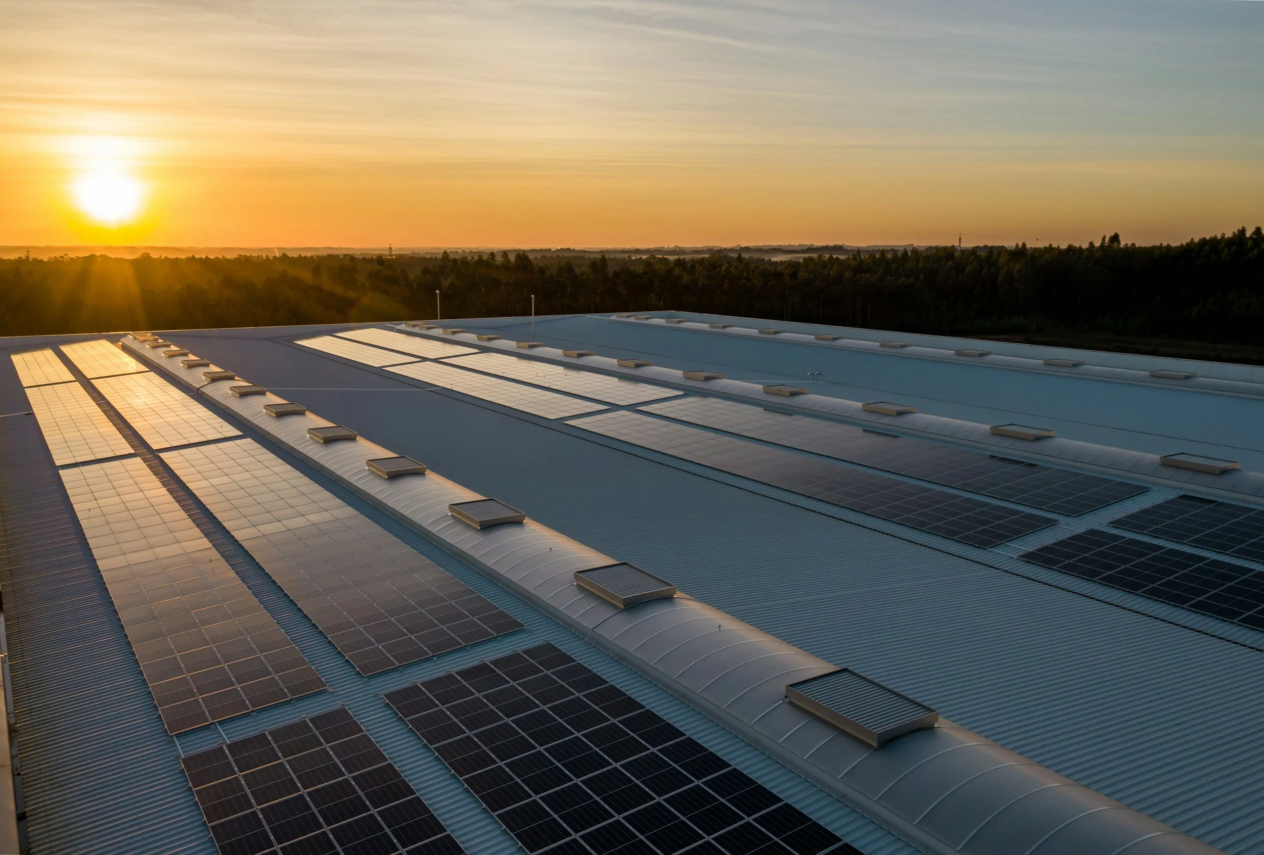 Sunset over a large industrial building with a roof covered in solar panels.