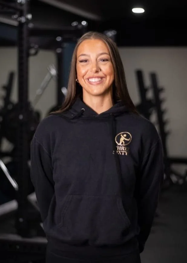 Smiling woman in black hoodie with gym logo in a fitness center.