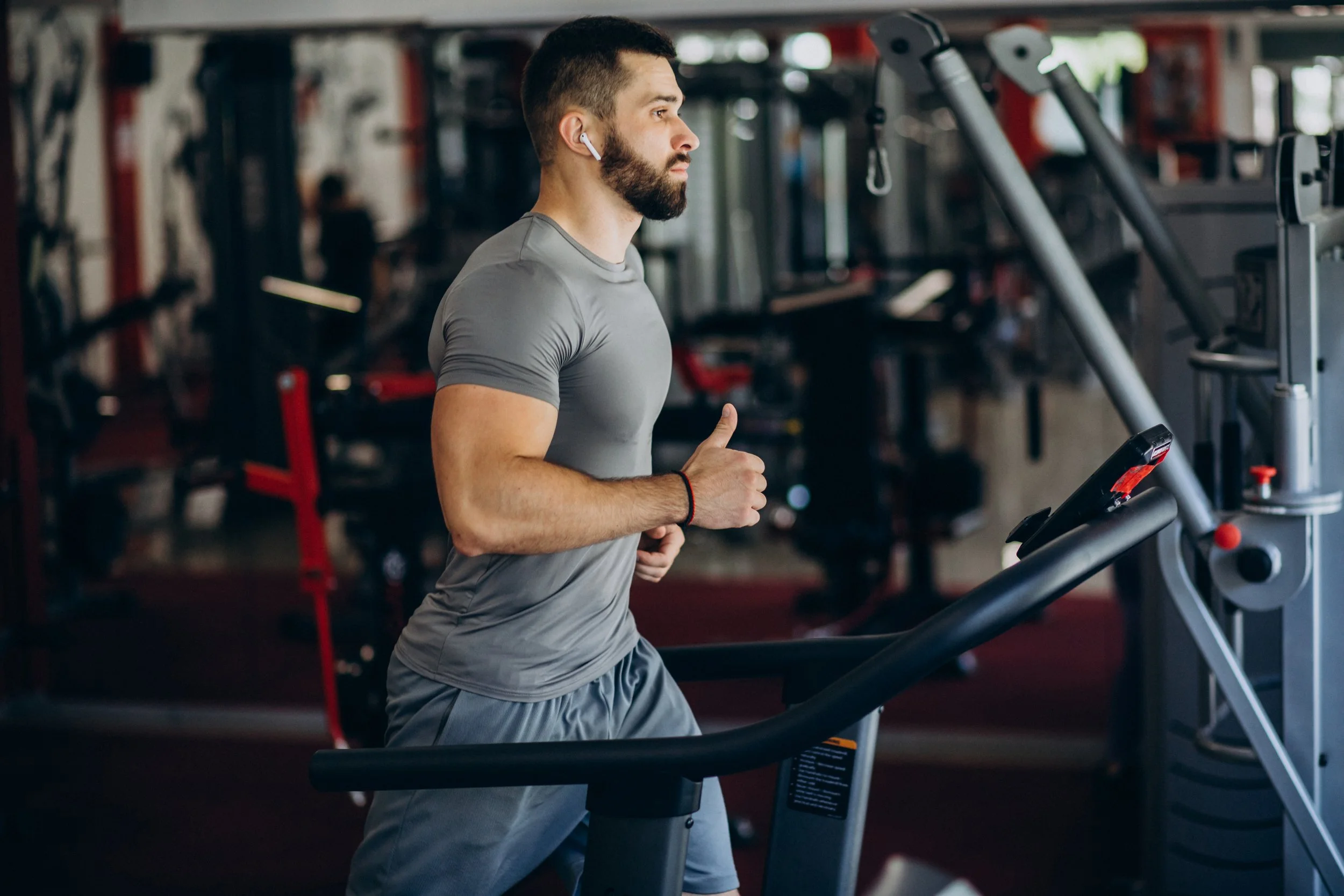 A man with a beard and earbuds running on a treadmill in a gym.