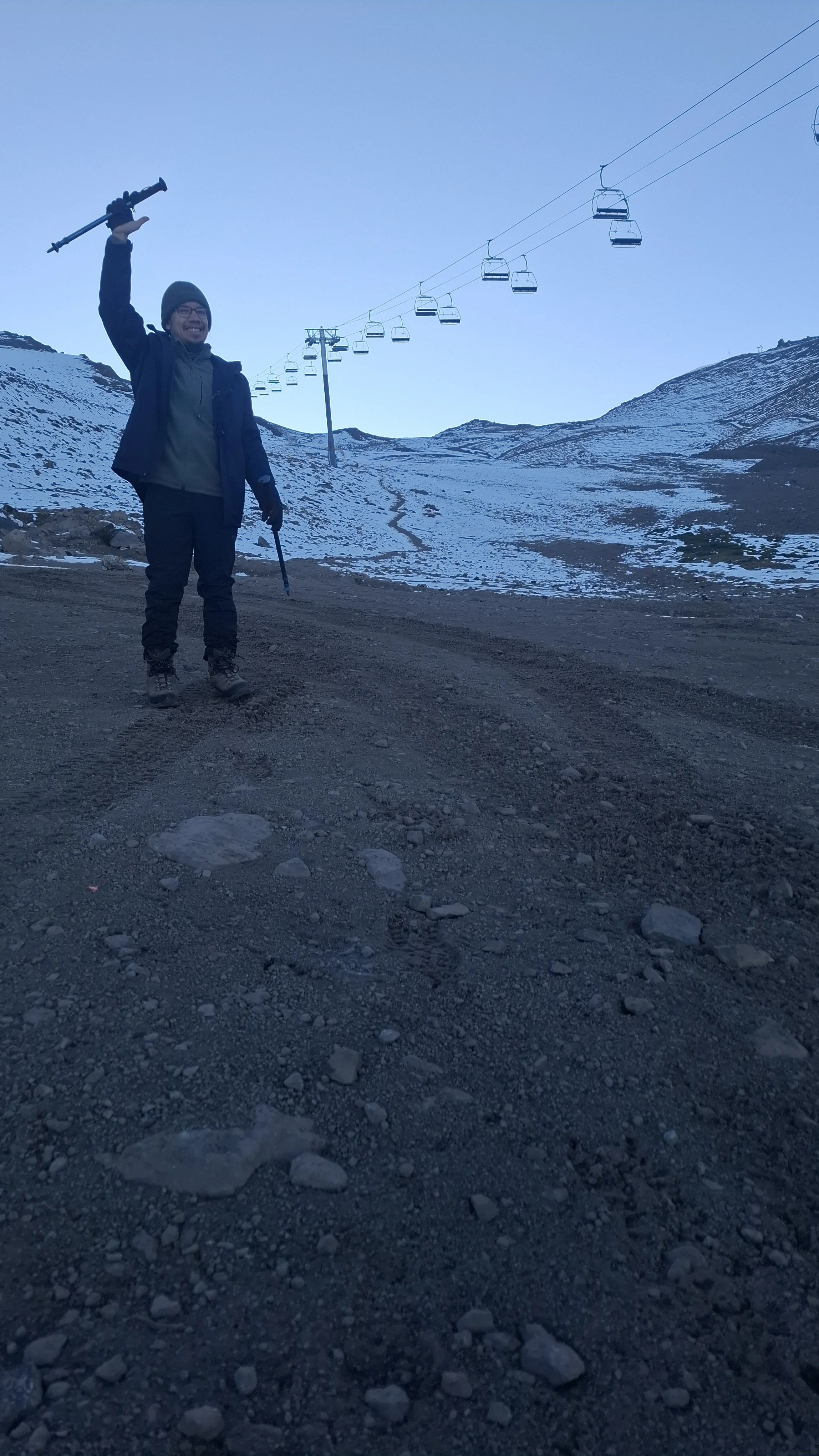 Persona sosteniendo un bastón en una montaña con nieve, cerca de un telesilla.
