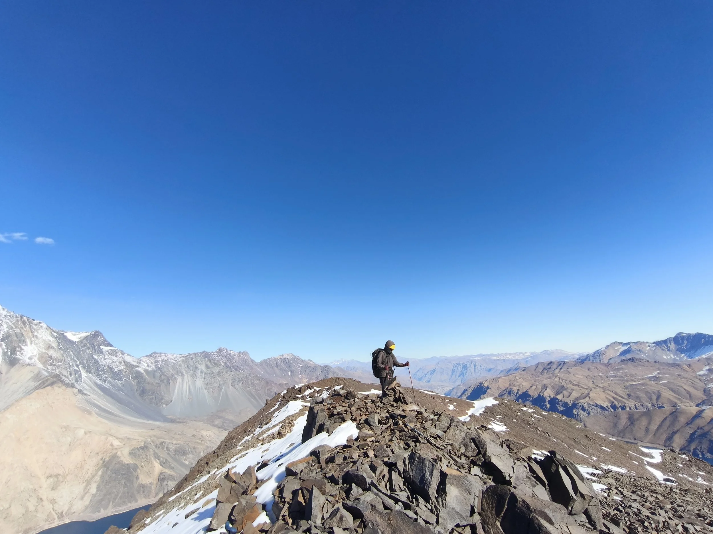 Persona escalando en una zona montañosa con picos nevados y cielo despejado