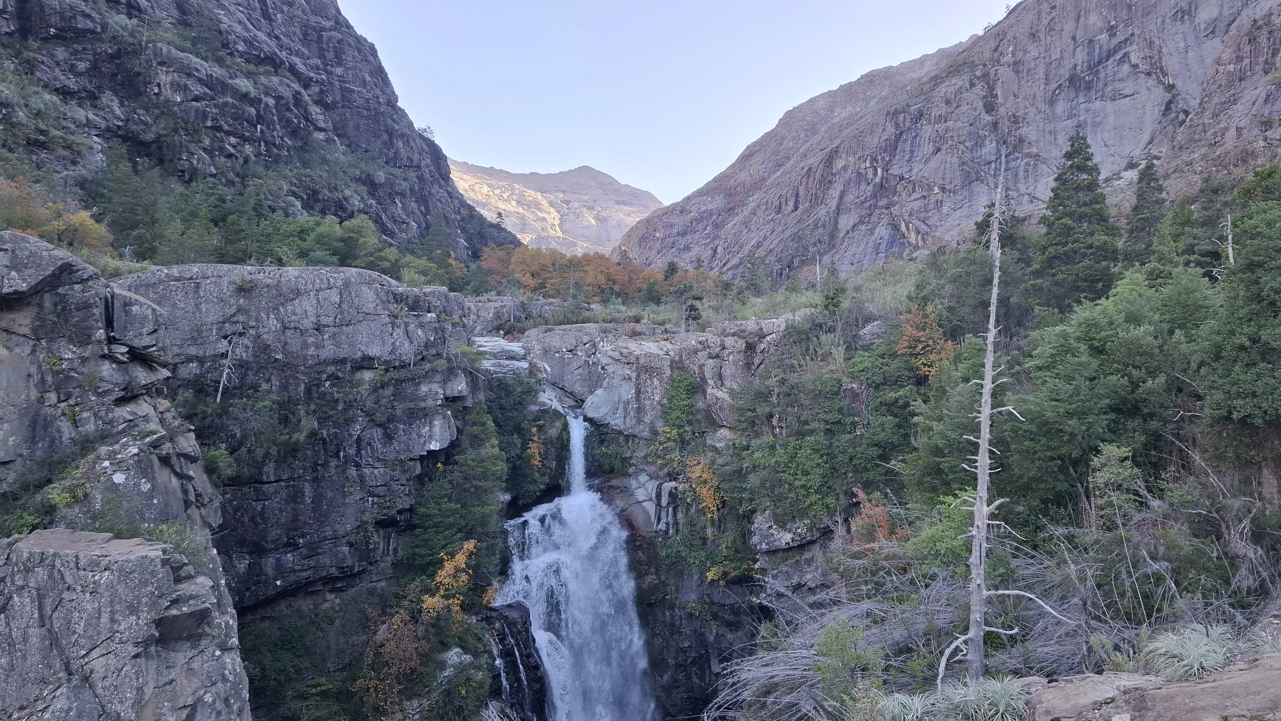 Cascada en un cañón rodeado de árboles y montañas rocosas.