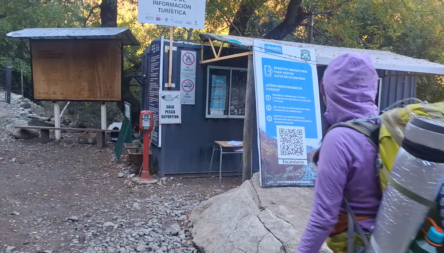 Cartel informativo y señalización en una zona de senderismo o parque natural, con una persona de espaldas con mochila y equipo de senderismo, entorno de árboles y caminos.