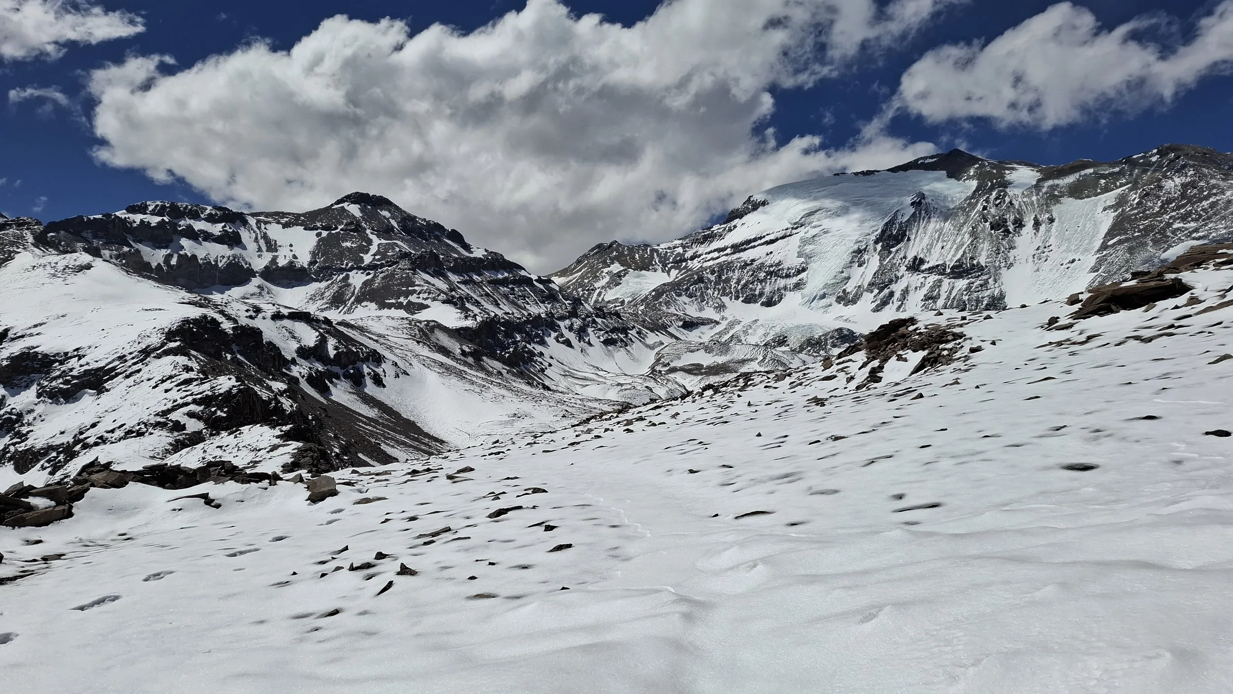 Montañas cubiertas de nieve con cielo nublado y algunas nubes blancas.