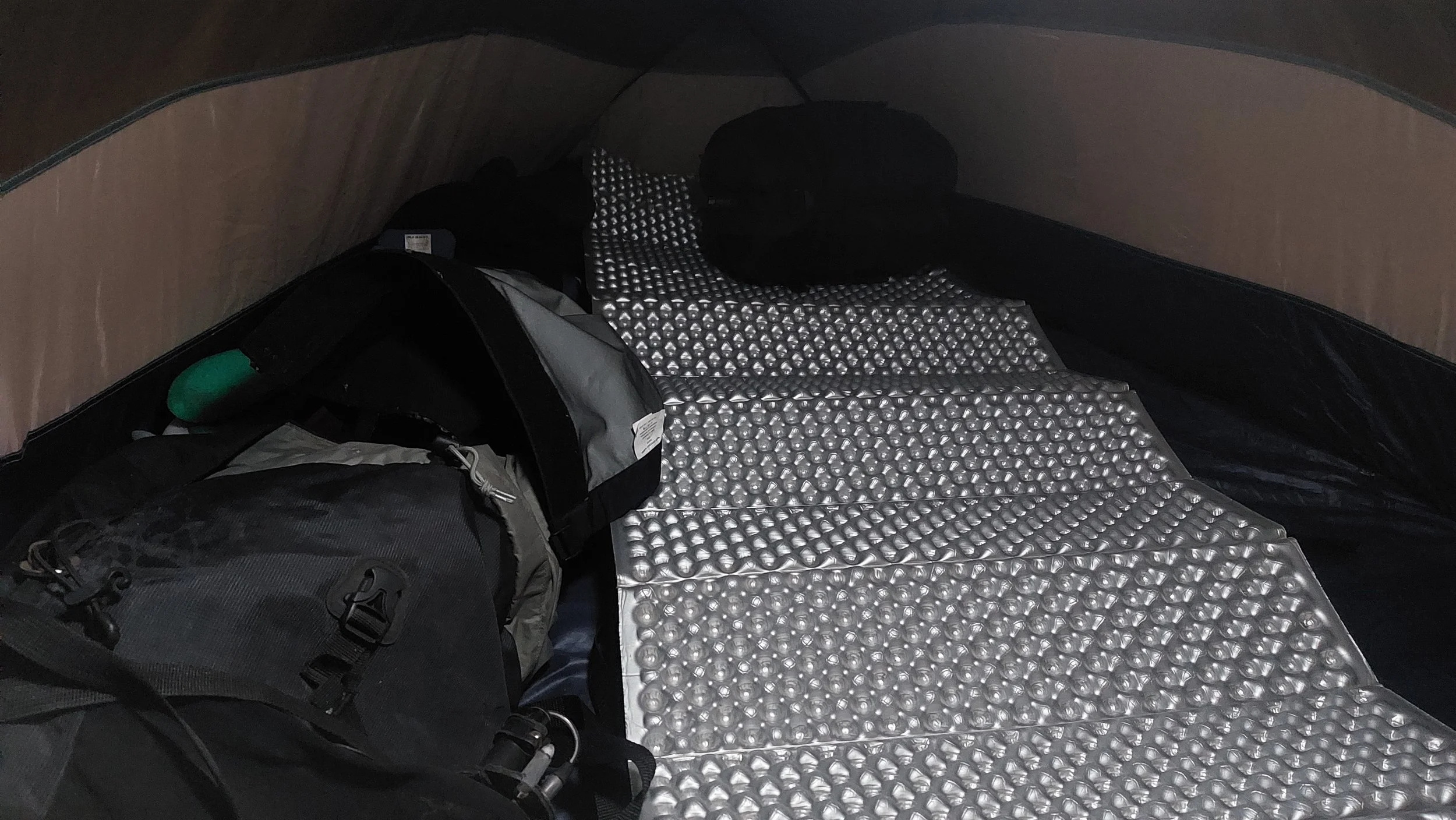 Interior de una tienda de campaña con bolsas, ropa y un colchón inflable