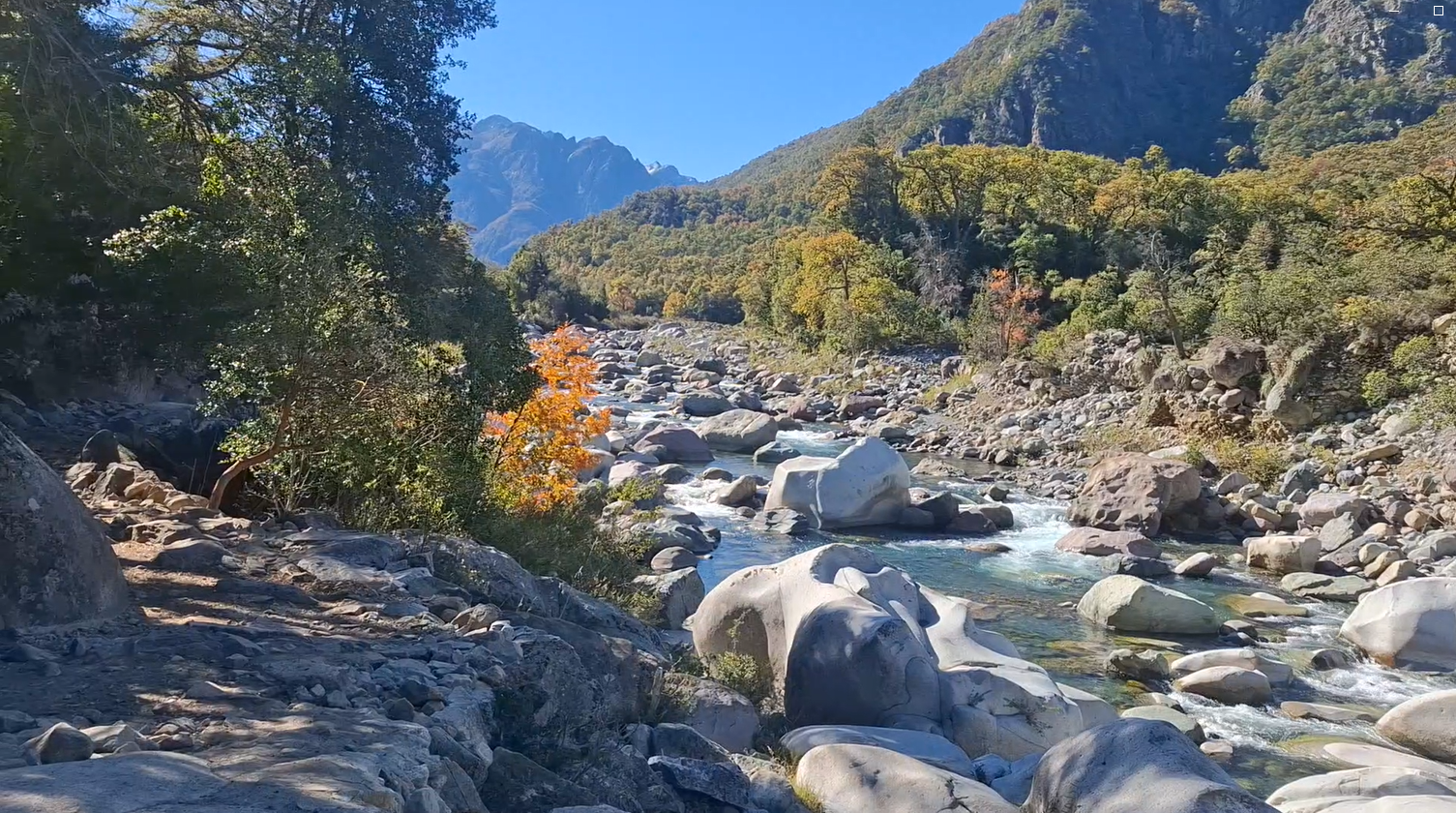 Vista de un río con rocas y árboles de otoño rodeado de montañas y una clara cielo azul.