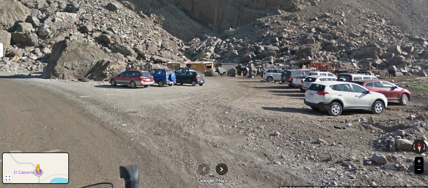 Estacionamiento en un área rocosa con varios autos y casas de madera en un entorno montañoso.