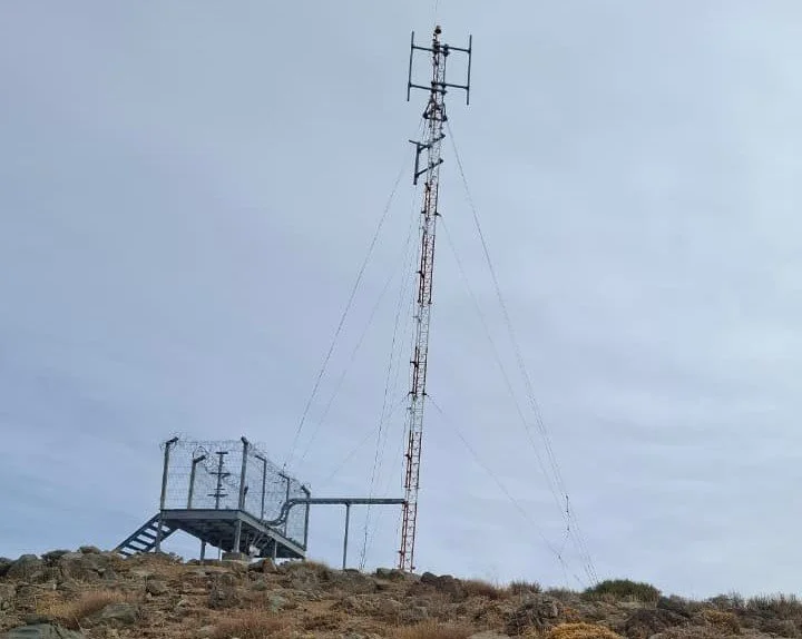 Antena de telecomunicaciones en un terreno rocoso con cielo nublado.