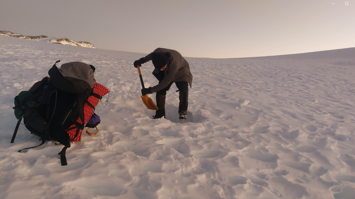 Persona con chaqueta y gorro haciendo alguna acción en la nieve con una pala en un paisaje helado.