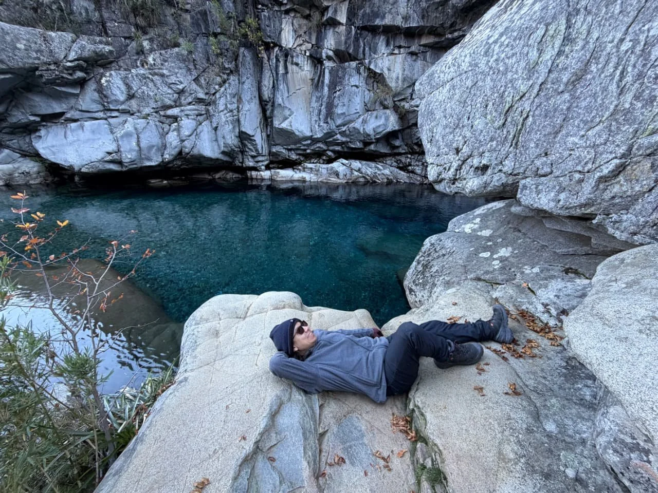 Persona descansando en una roca cerca de un cuerpo de agua en un cañón con paredes de piedra.