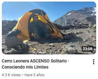 Persona en camping en un paisaje montañoso con picos nevados y cielo azul.