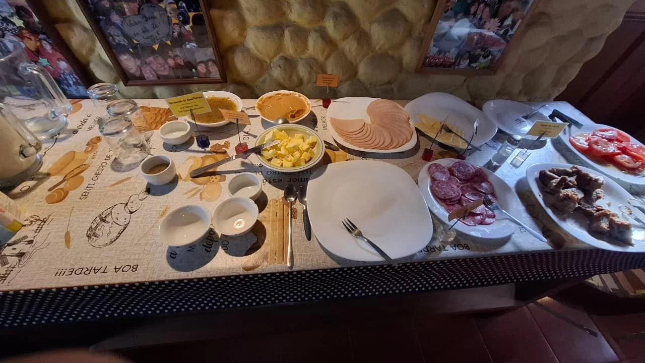Mesa de desayuno con varios alimentos fríos, como jamón, salami, carnes asadas, queso, tomate, fruta, y salsas.