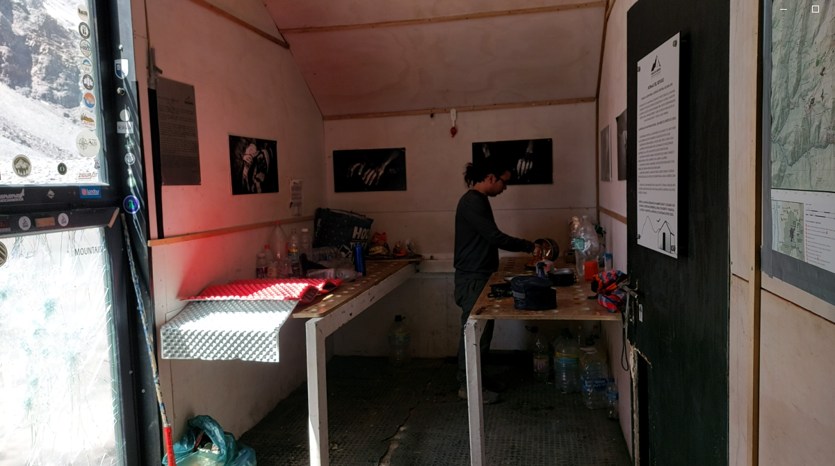 Una persona en una cabaña de madera sirviendo agua en el fregadero, con paredes adornadas con mapas y fotografías