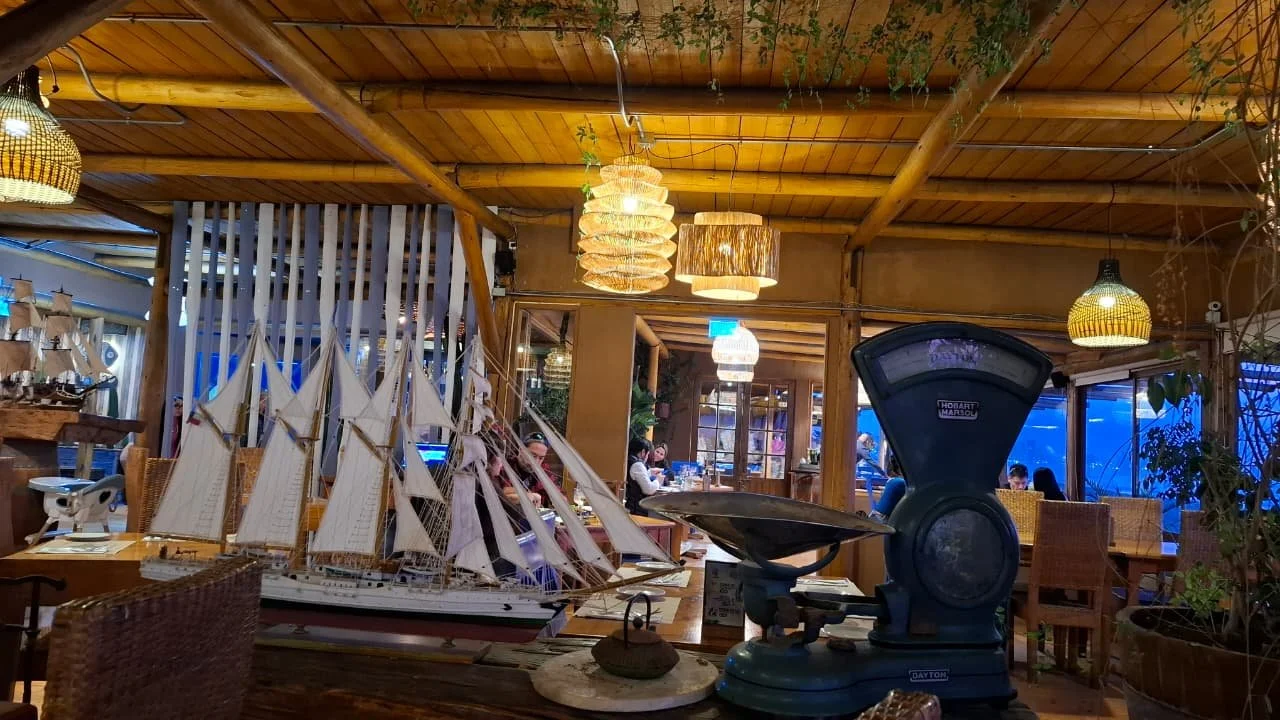 Interior de restaurante con maderas, lámparas de techo, escalas antiguas, detalles decorativos y un modelo de barco en la mesa