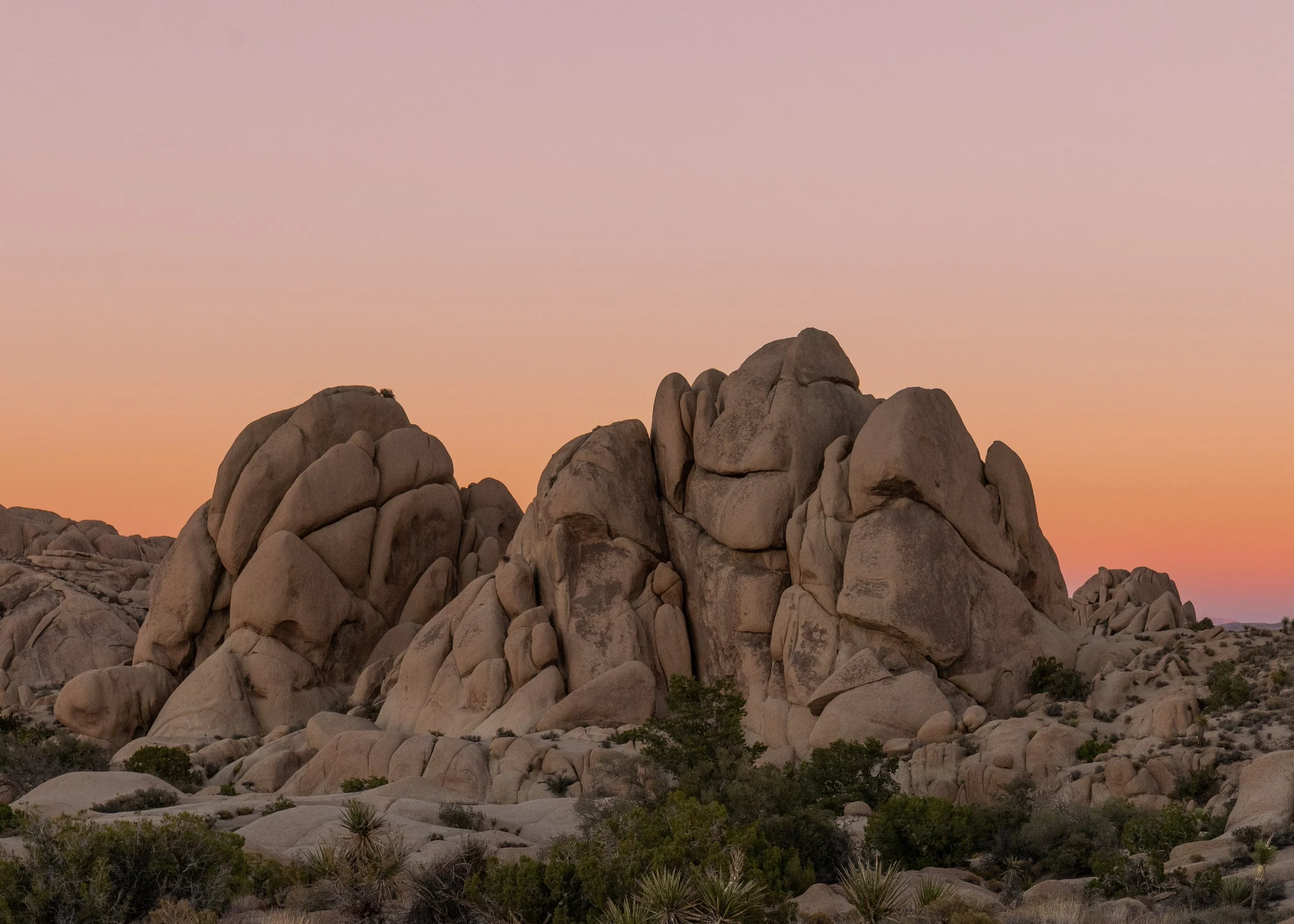 Large rock formations in a desert landscape at sunset with a colorful sky.