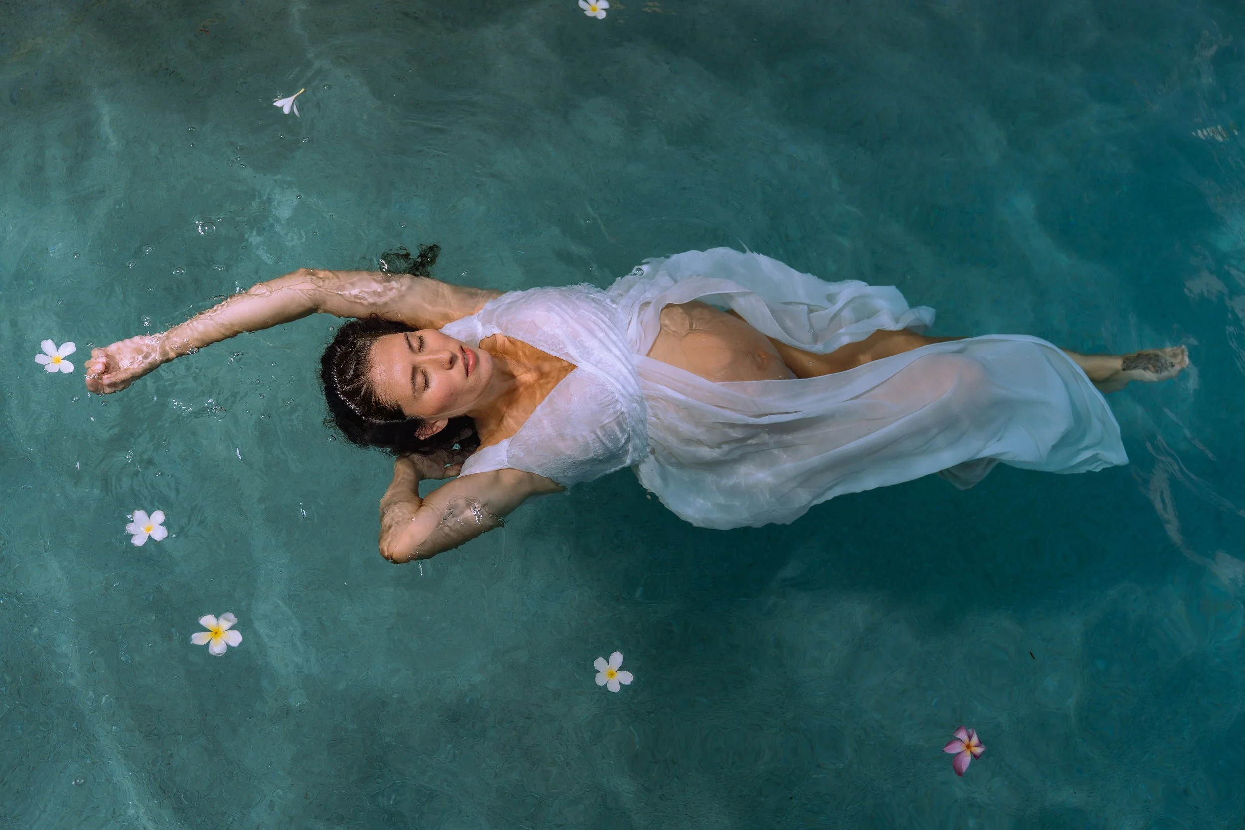 Woman in a white dress floating in a pool with flowers around her.