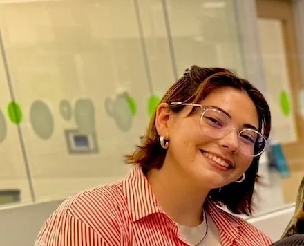 Chloe Regan is smiling warmly. She is wearing glasses and a red striped shirt.