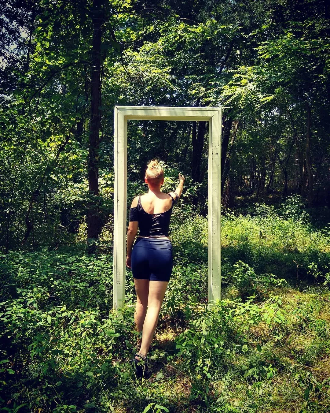 A figure (Tay Rogers) reaches toward an open doorframe in the woods, a portal of some kind.